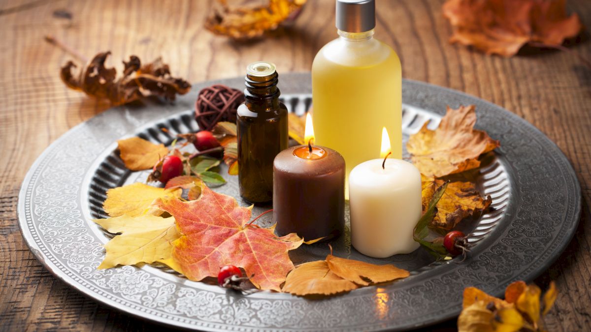 A decorative tray with candles, bottles, and autumn leaves, set on a wooden table, creating a cozy, seasonal ambiance.
