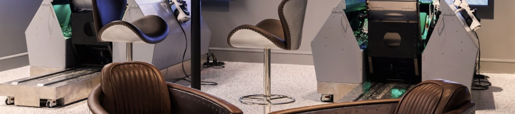 The image shows a modern room with two flight simulators, each in front of a screen, and several stylish chairs around them.