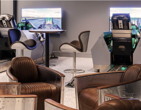The image shows a modern room with two flight simulators, each in front of a screen, and several stylish chairs around them.