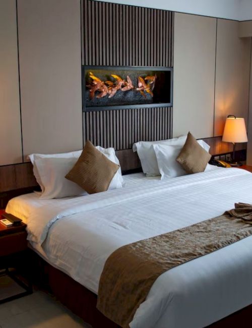 A neatly arranged bedroom with a large bed, two side tables with lamps, decorative pillows, and wall art, illuminated by natural and artificial light.