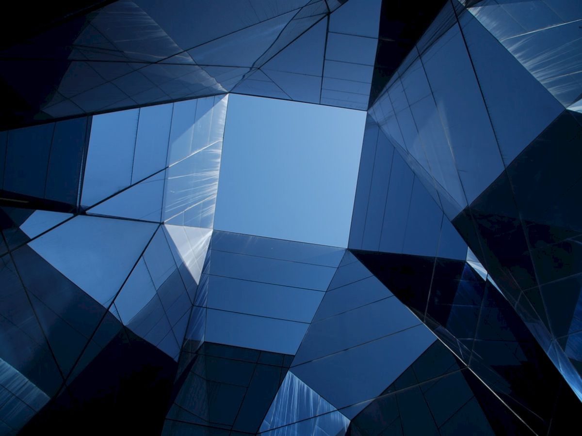 The image shows a geometric composition of glass and metal structures forming a polygonal frame, leading to an open sky view in the center.