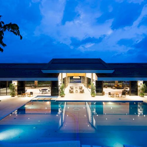 A modern building featuring expansive glass windows, a large reflecting pool, and a scenic outdoor area illuminated at dusk.