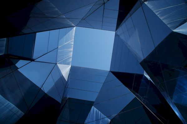 A view from the ground upwards, showing modern, reflective buildings forming a geometric pattern against a clear blue sky.