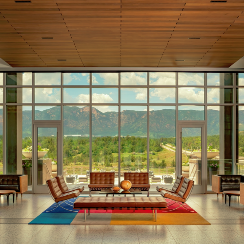 A modern lobby with stylish furniture sits before large windows overlooking a scenic mountain view, complemented by a colorful geometric rug.