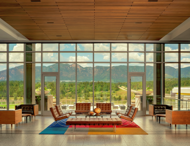 A modern lobby with stylish furniture sits before large windows overlooking a scenic mountain view, complemented by a colorful geometric rug.