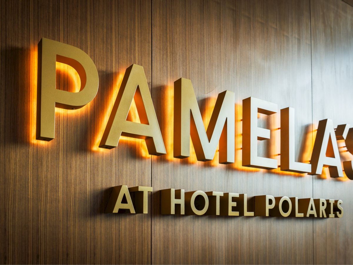 The image shows a sign reading "PAMELA'S AT HOTEL POLARIS" on a wooden wall, with illuminated letters.