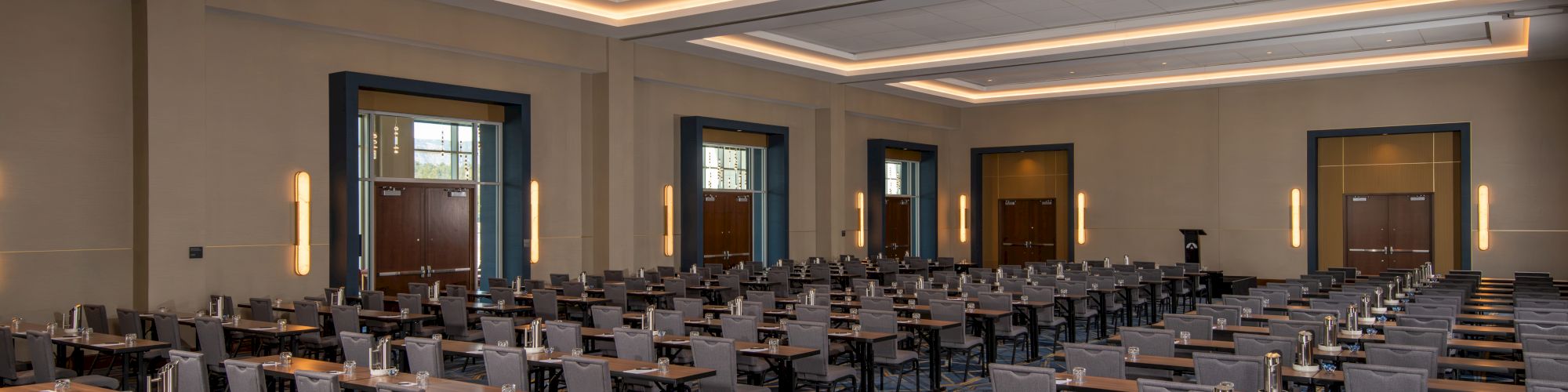 The image shows a large conference room with rows of tables and chairs, set up with notepads and water pitchers on the tables.