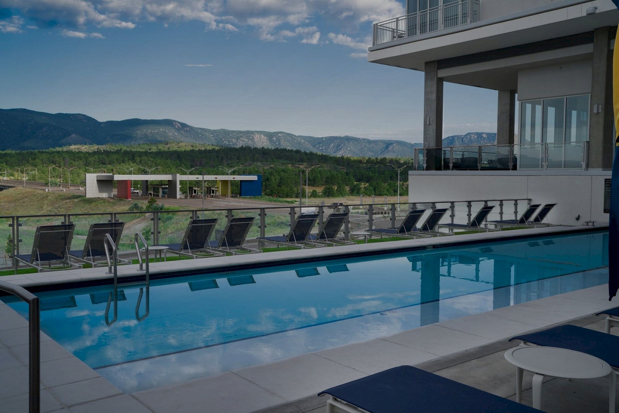 A modern rooftop pool with lounge chairs, glass railing, and a scenic mountain view beyond the deck. Ends with a period