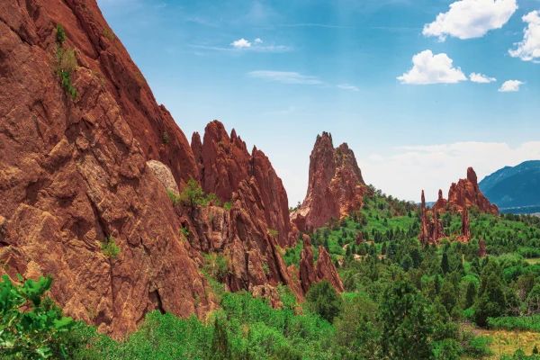 The image shows a scenic landscape featuring large red rock formations, green vegetation, and a bright blue sky with a few clouds ending the sentence.