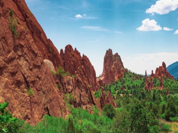 The image shows a scenic landscape featuring large red rock formations, green vegetation, and a bright blue sky with a few clouds ending the sentence.