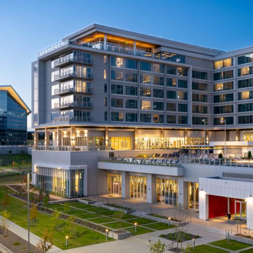 A modern multi-story office and campus-style building complex with glass walls, walkways, and manicured landscaping, on a clear day.