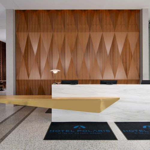 A hotel lobby interior with a modern reception desk, wooden accents, and unique wall design. Mats read "Hotel Polaris."
