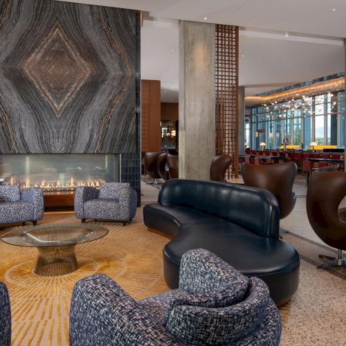 A modern lounge with a fireplace, stylish seating, a patterned wall, and large windows offering a view outside.