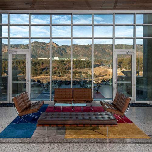 Modern interior with brown leather seating, large windows offering a stunning mountain view, and colorful square rugs on the floor.