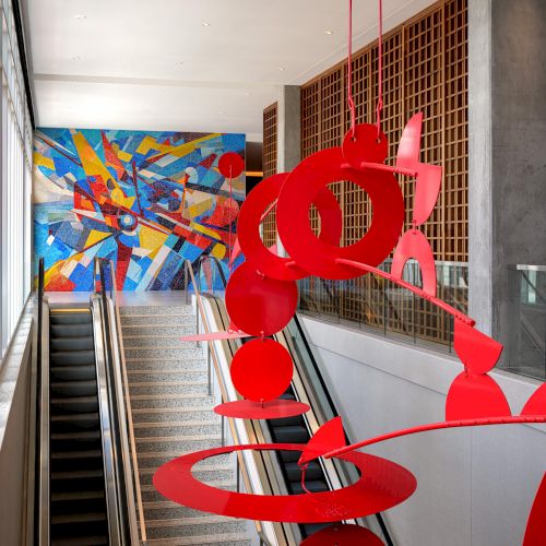 A bright, red metal sculpture on a staircase, with colorful artwork in the background.