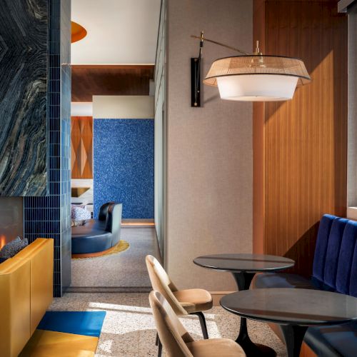 A mid-century modern living space with a wooden chair, blue walls, a sunlit doorway, and a warm beige couch near a small desk.