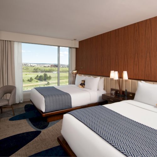 The image shows a hotel room with two double beds, a large window, and a view outside.