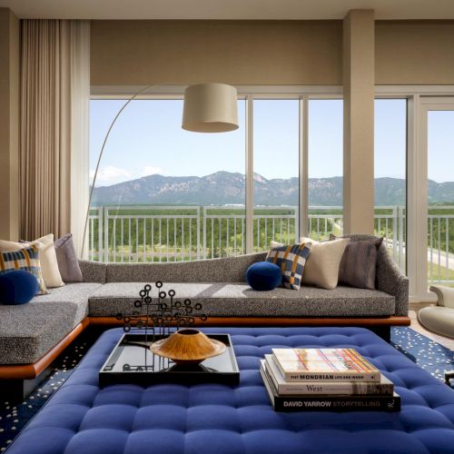 A luxurious living room with a panoramic balcony view, cozy seating, and a blue tufted ottoman centerpiece, perfect for relaxing and entertaining.