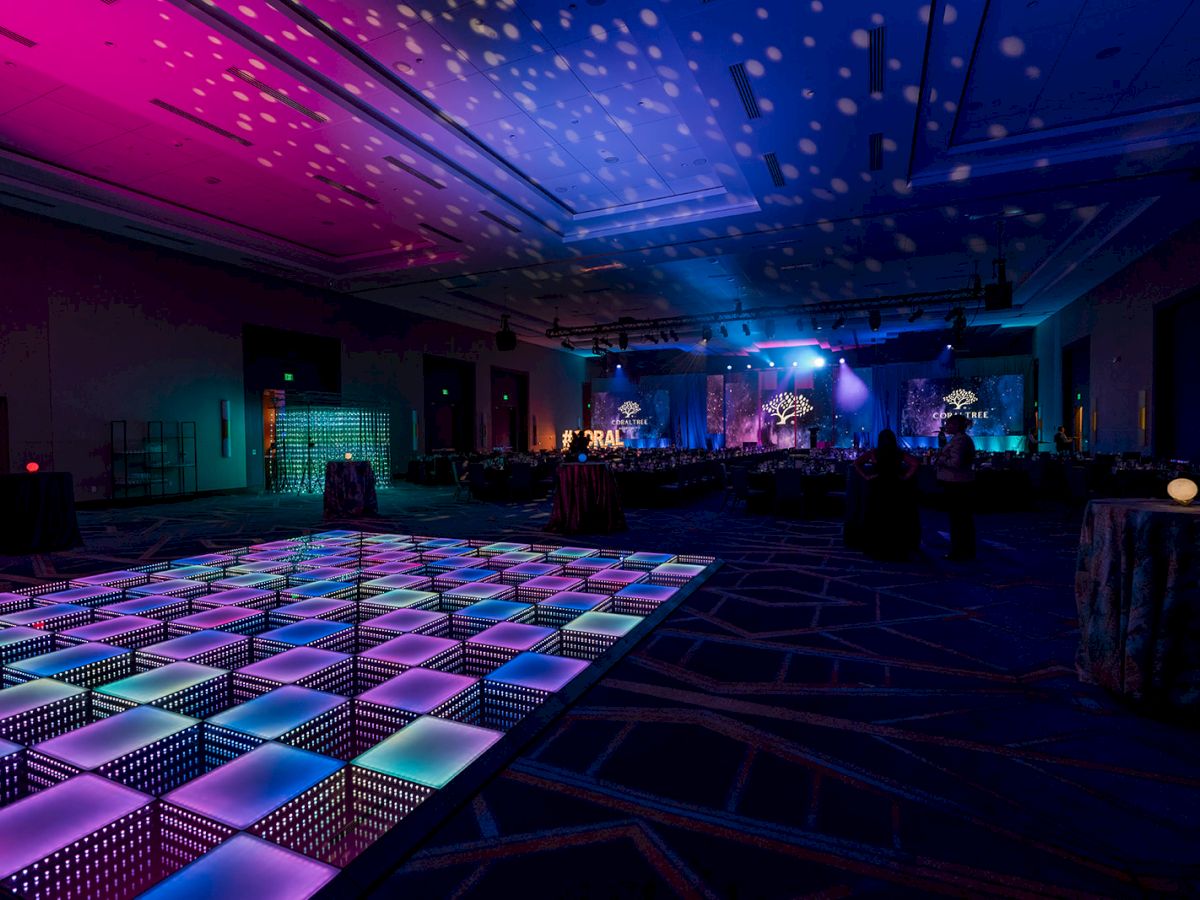 A dimly lit event space with a colorful LED dance floor and decorative lighting creating a festive atmosphere.