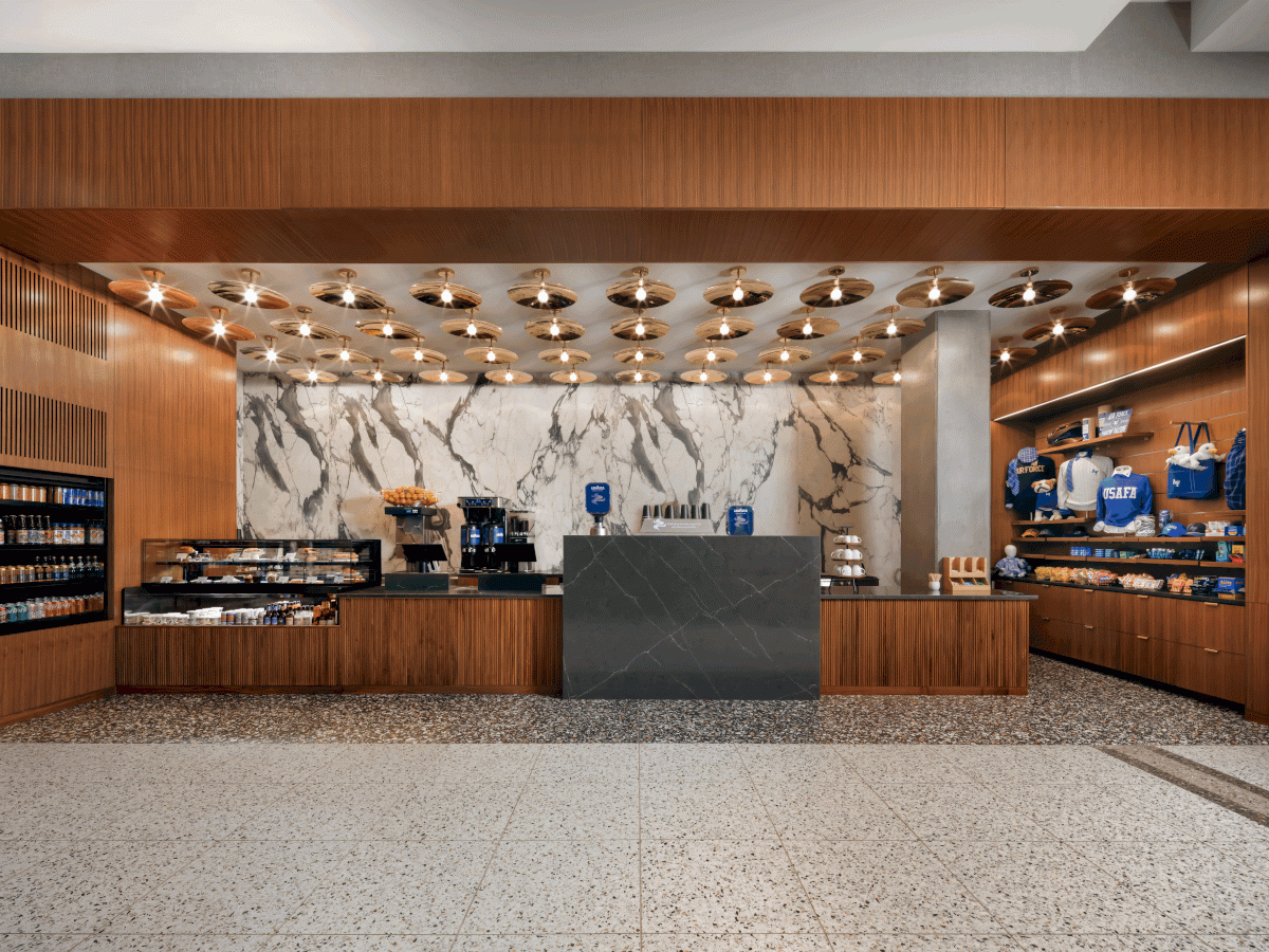 A modern café with a marble wall, wood accents, and shelves displaying blue coffee products, featuring a central counter and ceiling lights.