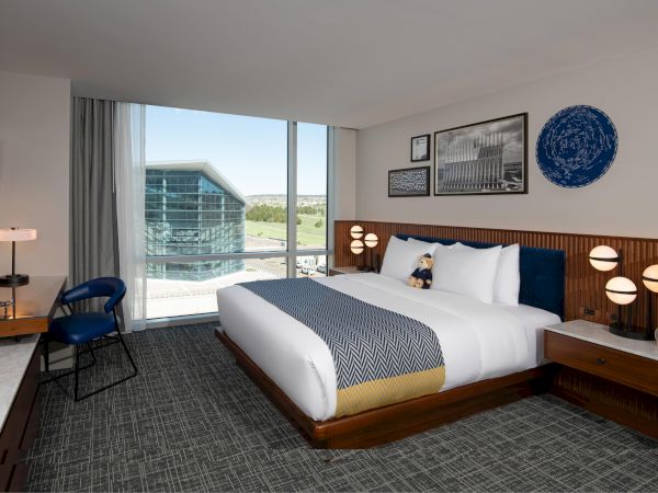 A modern hotel room with a large bed, stylish lamps, and a scenic window view of a building.