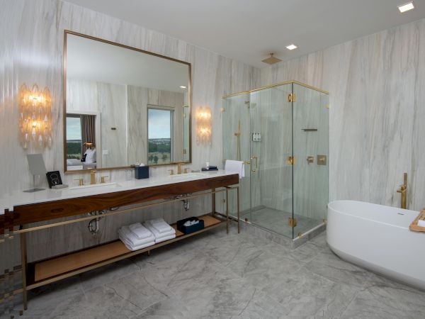 A modern bathroom with a glass shower, large mirror, dual sinks, and a standalone tub on a marble floor.