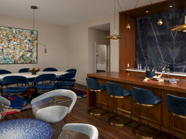 A modern dining area with velvet chairs, abstract art, a wooden bar, and a mosaic table. Elegant lighting and a cozy atmosphere.