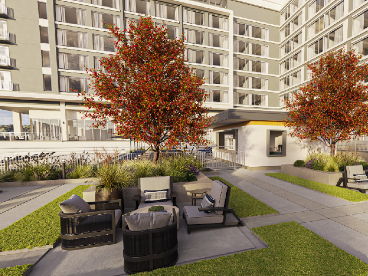The image features an outdoor patio area with lounge furniture and two trees with red leaves, set against the backdrop of a multi-story building.