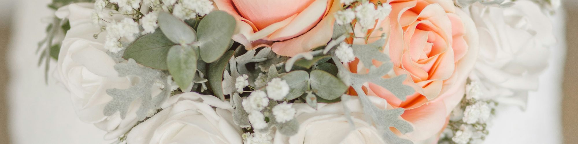 A person in a white dress is holding a bouquet of pink and white roses with greenery. The focus is on the flowers in the bouquet.