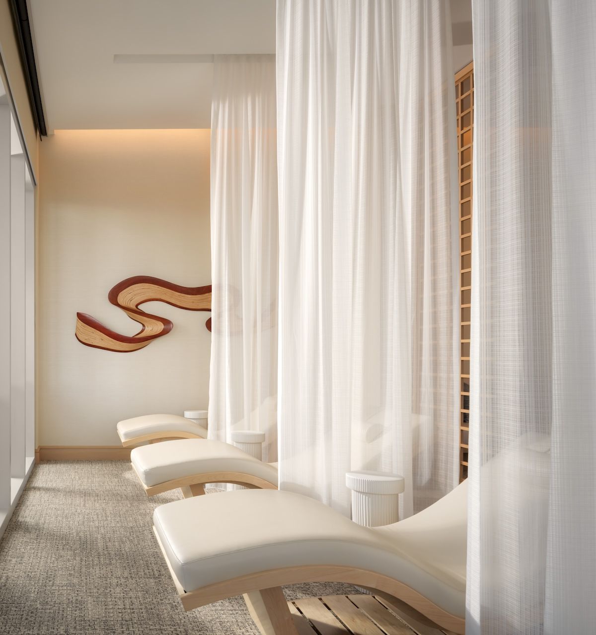 A serene spa or salon with white curtained sections, curved white lounge chairs, soft lighting, and abstract wall art in the background.
