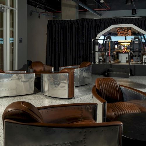 The image shows a room with leather chairs and a flight simulator cockpit in the background, creating an aviation-themed space.