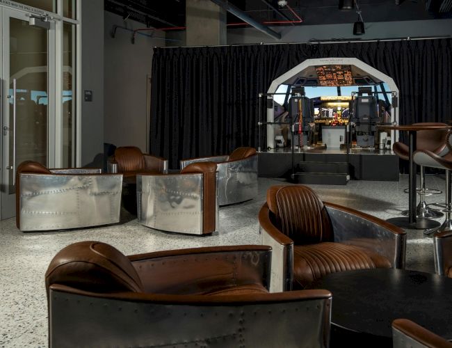 The image shows a room with leather chairs and a flight simulator cockpit in the background, creating an aviation-themed space.