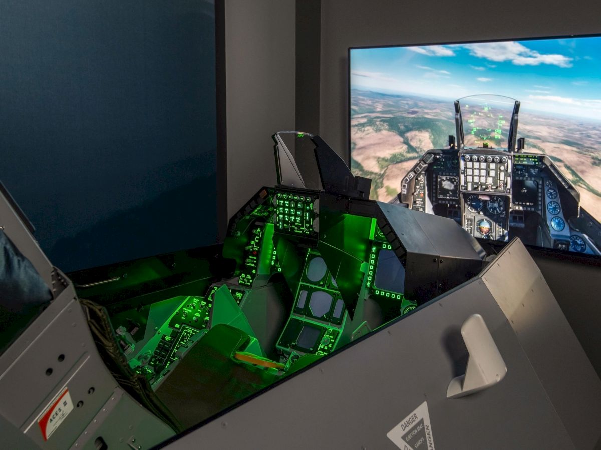 The image shows an aircraft simulator cockpit with illuminated controls and a screen displaying a virtual flight scene.