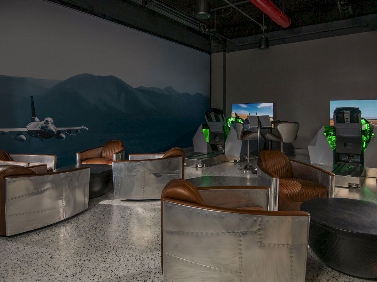 The image shows a room with flight simulators, sleek leather chairs, and aviation-themed decor, including a large fighter jet mural.