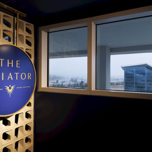 A sign reading "The Aviator" is on a wall beside windows showing a modern building outside.
