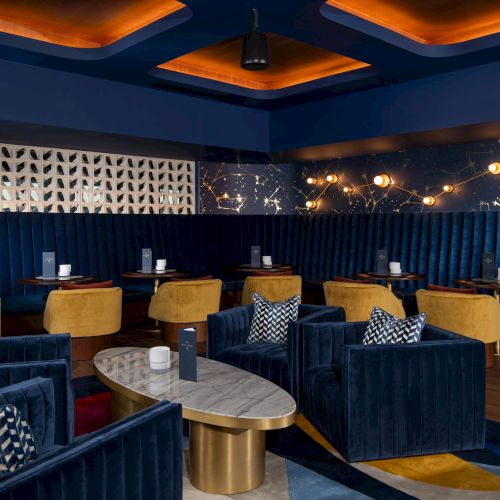 Luxurious lounge with blue and mustard seating, geometric patterns, a marble table, and constellation-themed wall decor.