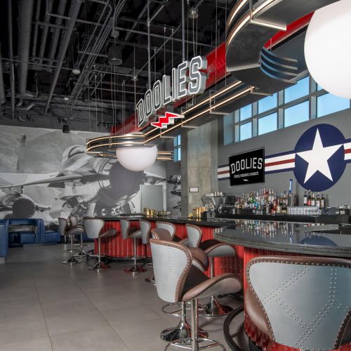 A stylish bar with aircraft-themed decor, featuring stools, tables, and a sign saying "Doolies" above the counter.