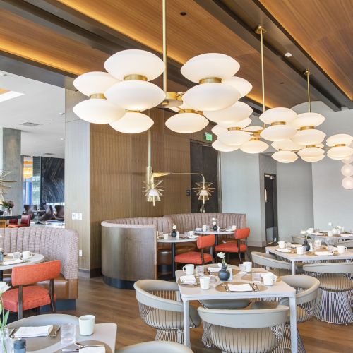 Modern dining area with stylish chandeliers, tables set with dishes, plush seating, and a large wall mirror reflecting the space.