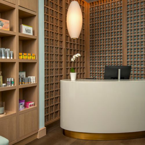 A modern reception area with a curved desk, a computer, shelves with products, and a potted orchid, featuring wooden lattice walls.