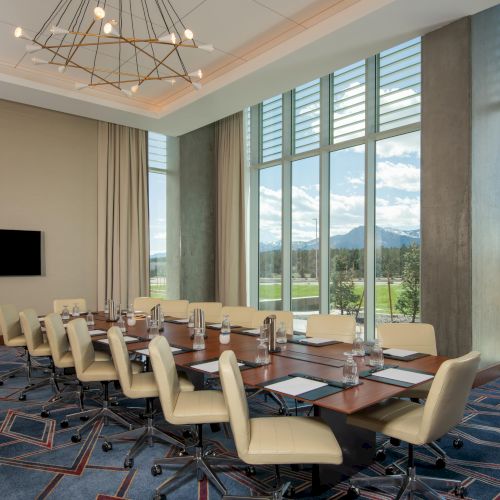 A conference room with a large table, chairs, a TV on the wall, and a view of a scenic landscape through large windows.