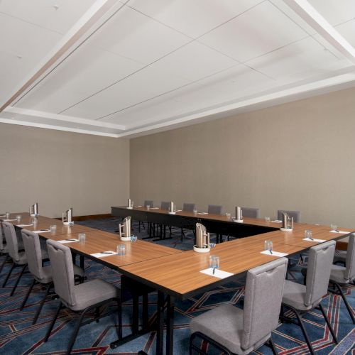 A conference room with arranged tables and chairs in a U-shape layout, featuring notepads, pens, and water glasses on the tables.
