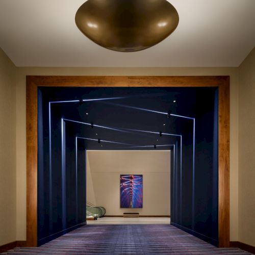 A long, blue-walled corridor with lighter floor tiles and framed doorways receding into the distance, ending in a distant doorway.