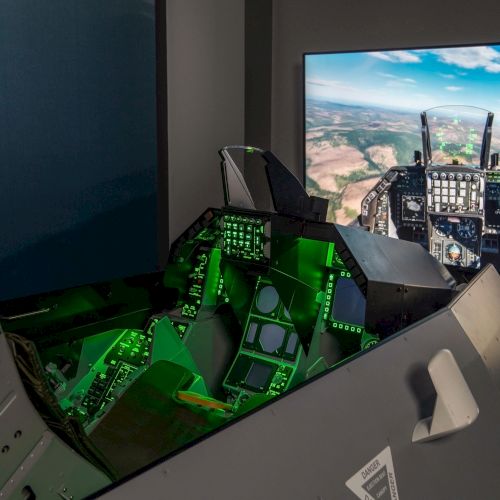 The image shows a flight simulator cockpit setup with glowing controls and a large screen displaying a flight view.