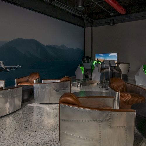 The image shows a flight simulator room with simulator setups, leather chairs, metal furniture, and a wall mural of a jet in flight.