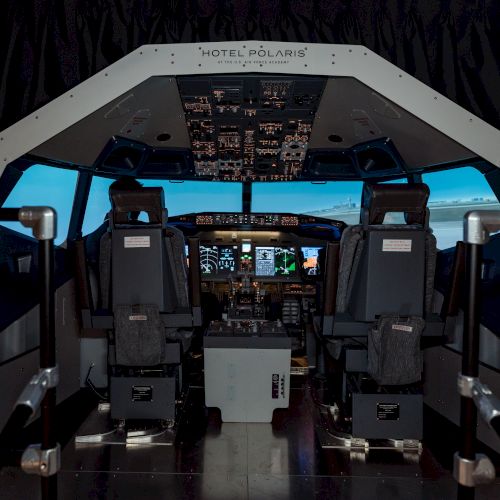 The image shows a flight simulator cockpit with multiple controls, screens, and seating for pilots, likely used for training purposes.