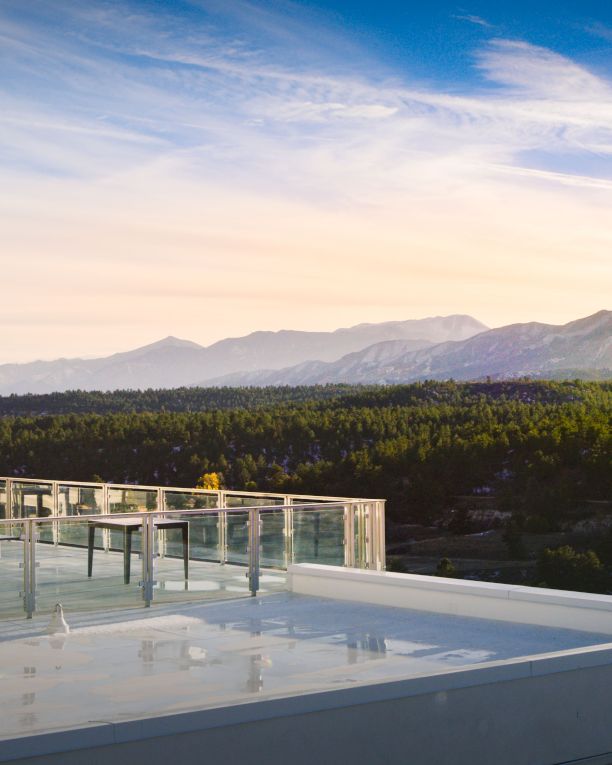 A modern rooftop terrace with glass railing overlooks a valley and distant mountains at sunset, clean lines, calm and expansive.