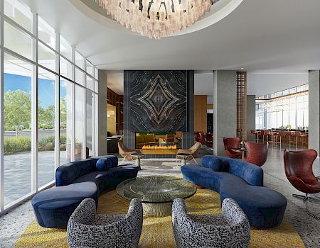 A modern lounge with curved sofas, armchairs, a central table, large windows, unique chandelier, and a decorative fireplace feature.