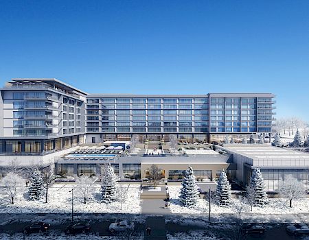 A modern multi-story building in a snowy landscape, with trees in the foreground and mountains in the background.