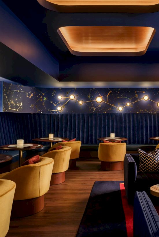 A stylish lounge with blue velvet seating, warm lighting, and round tables; cozy, upscale bar vibe.