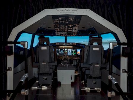 The image shows an aircraft cockpit simulator with two seats, complete with controls and screens, designed for pilot training experiences.